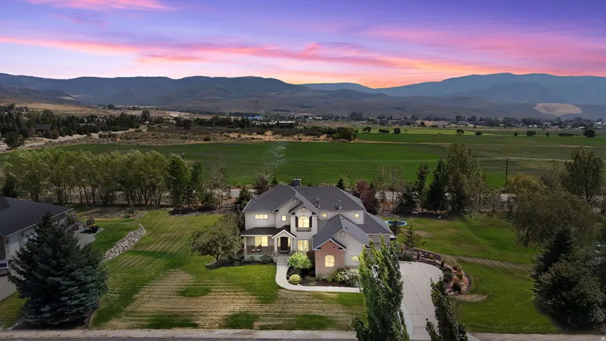 Gabled roofline, stone and siding exterior, front porch, mature landscaping, and an expansive paved driveway