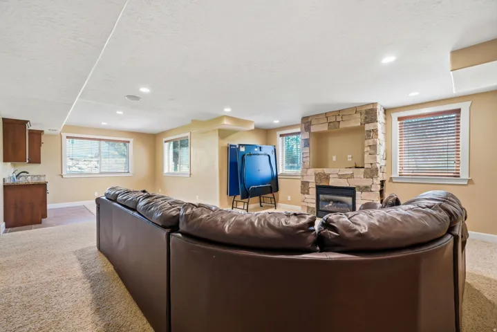 Recessed lighting, stone-clad fireplace, built-in wet bar with cabinetry, carpeted flooring, and multiple windows