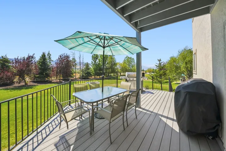 Expansive wood-finish deck with black metal railings, covered patio area, and lush green landscaping