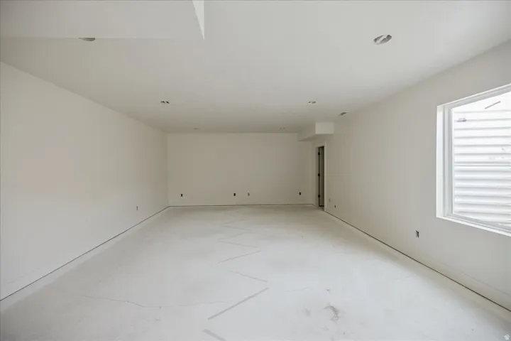 Spacious room featuring white painted walls and ceiling, recessed lighting, and a white framed window