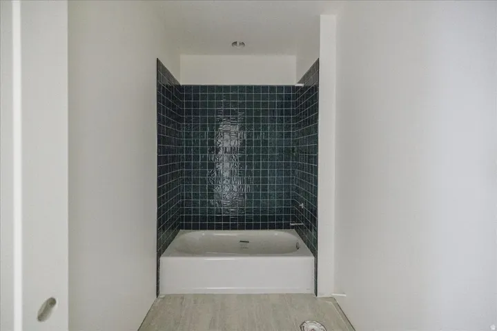 Built-in bathtub with subway tile surround and light wood-finish flooring