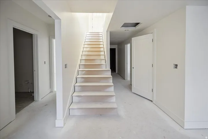 Entryway featuring a straight staircase with carpeted treads, smooth white walls, white trim, and light-colored flooring