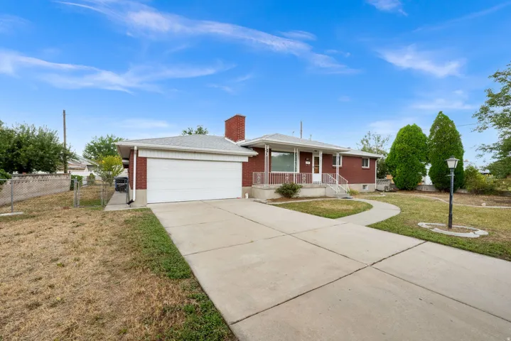 Red brick exterior, attached garage, concrete driveway, front porch with white railing, and a mature tree