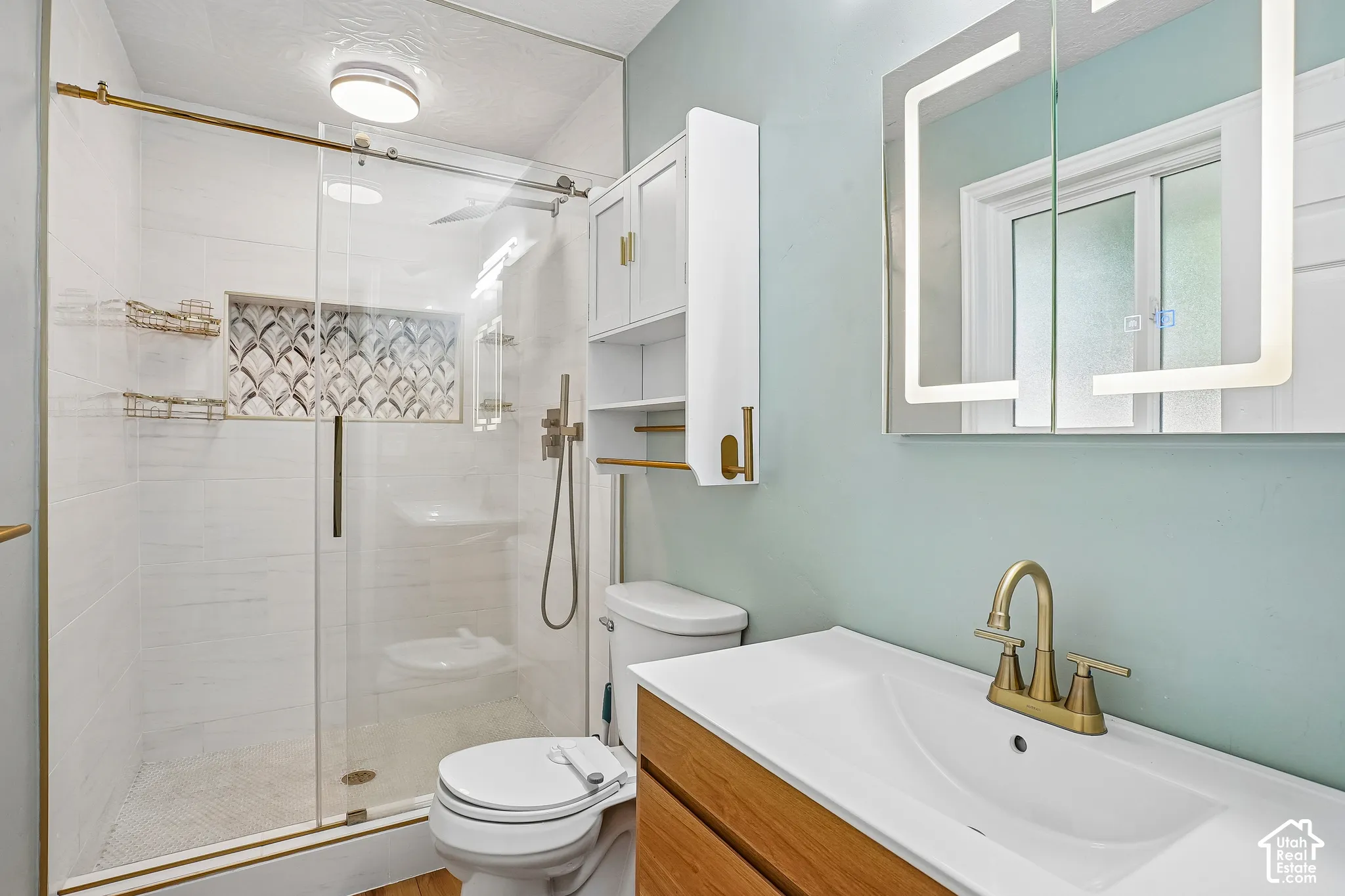 Walk-in shower with glass enclosure, decorative tile accent, and gold-toned fixtures