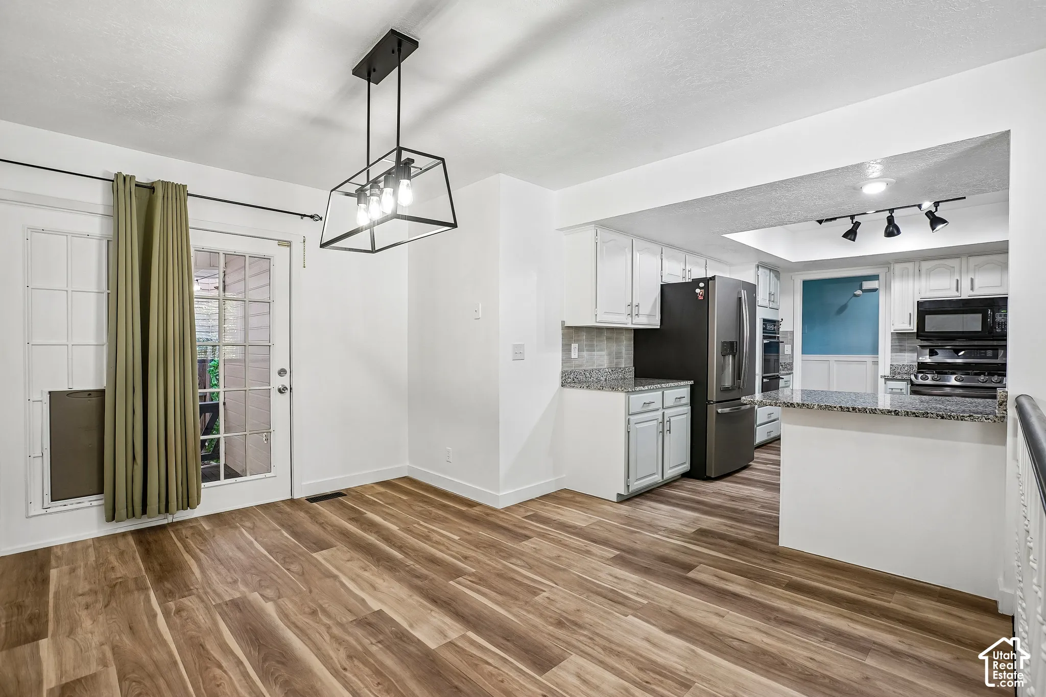 Wood-finish flooring, white cabinetry, granite countertops, stainless steel appliances, and a modern geometric pendant light fixture