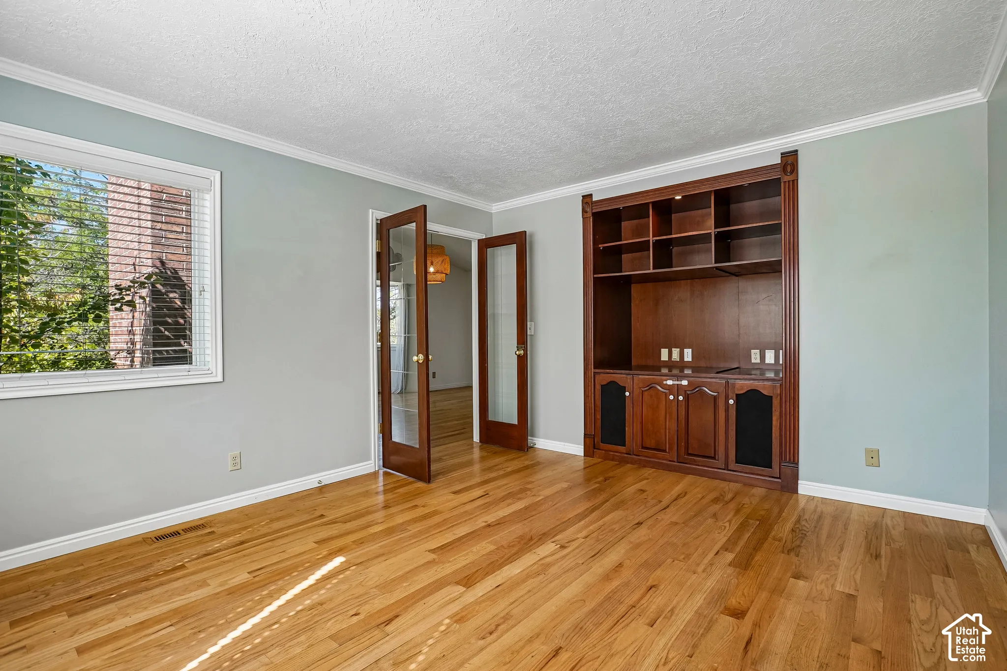 Hardwood flooring, built-in shelving, built-in cabinetry, French doors with glass panels, and crown molding