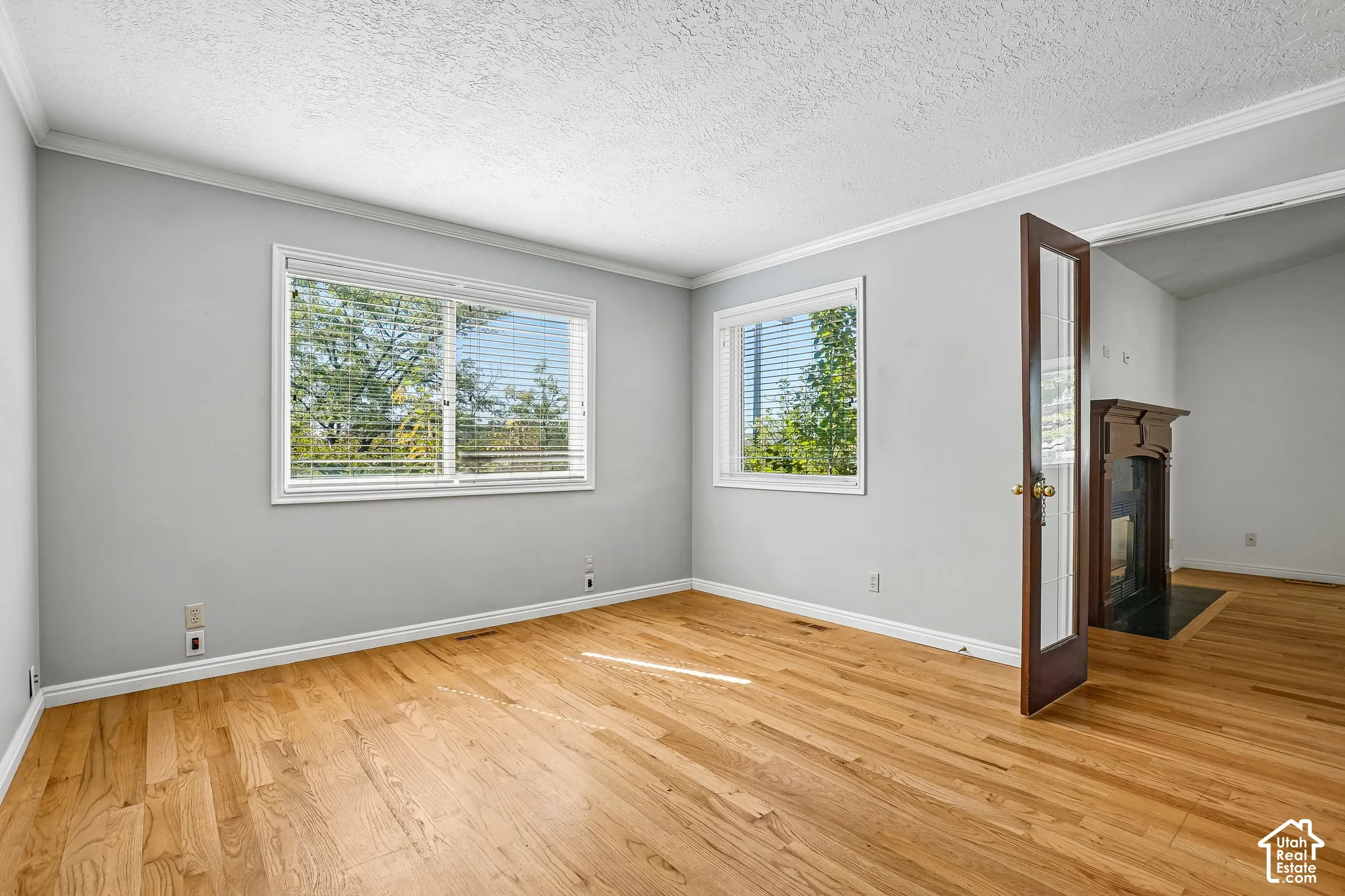 Hardwood flooring, crown molding, double windows with blinds, and a dark wood-finish mantel with a black hearth