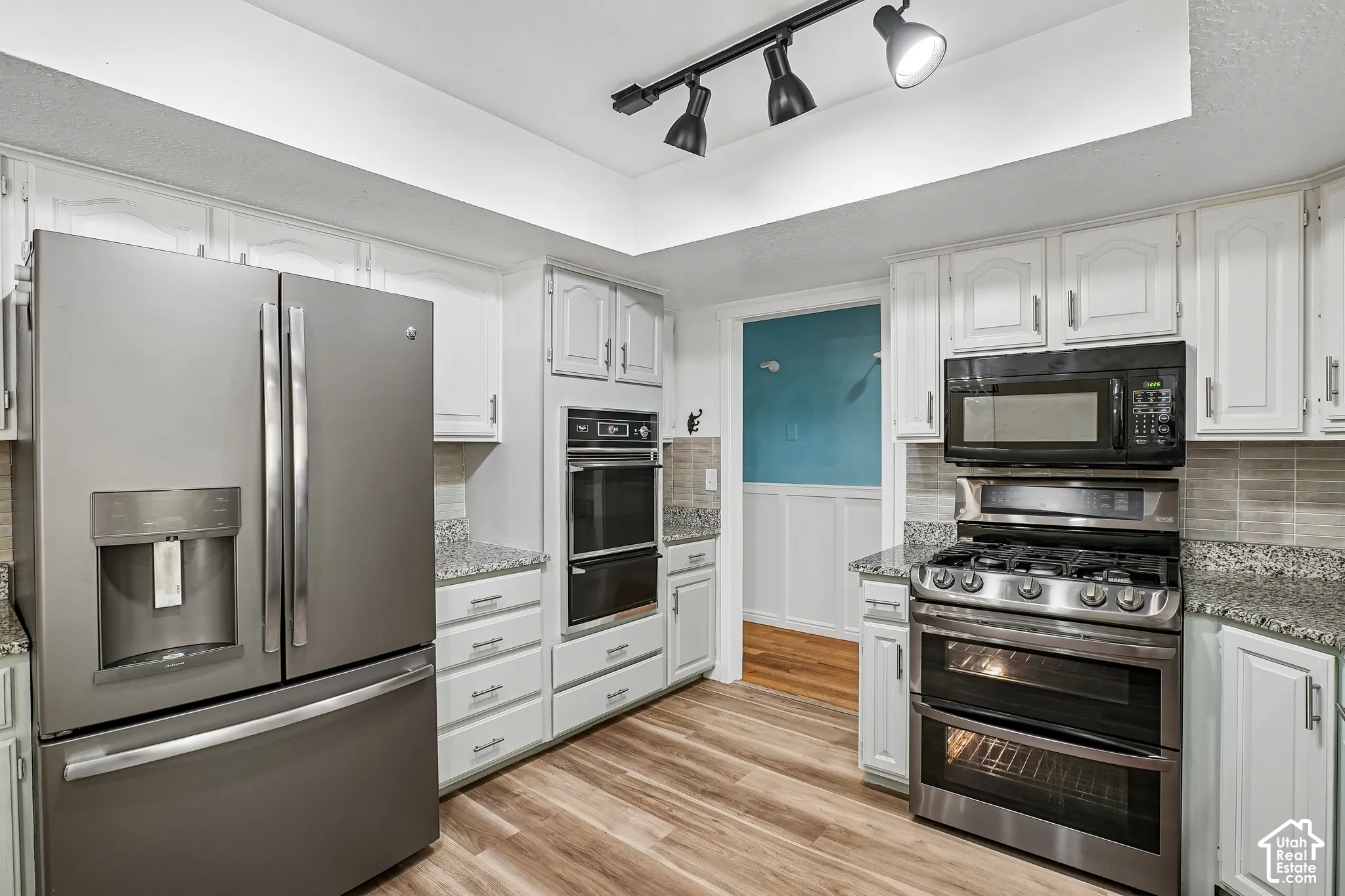 White cabinetry, wood-finish flooring, stainless steel appliances, granite countertops, and tile backsplash