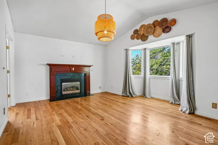 Vaulted ceilings, wood-finish flooring, a fireplace with a wood mantel and stone surround, and a bay window