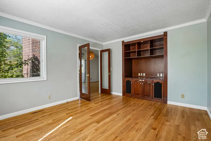 Hardwood flooring, built-in shelving, built-in cabinetry, French doors with glass panels, and crown molding