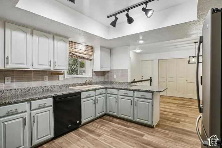 Kitchen featuring wood-finish flooring, two-tone cabinetry, granite-style countertops, a tile backsplash, and a built-in dishwasher