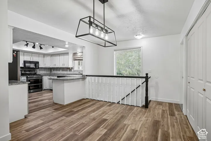 Wood-finish flooring, white cabinetry, dark stone-finish countertops, black appliances, and a contemporary linear chandelier