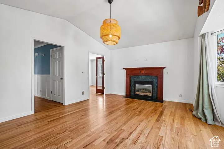 Vaulted ceiling with an overhead light fixture, wood-finish flooring, a fireplace featuring a wood mantel and tiled surround, and a window providing natural illumination