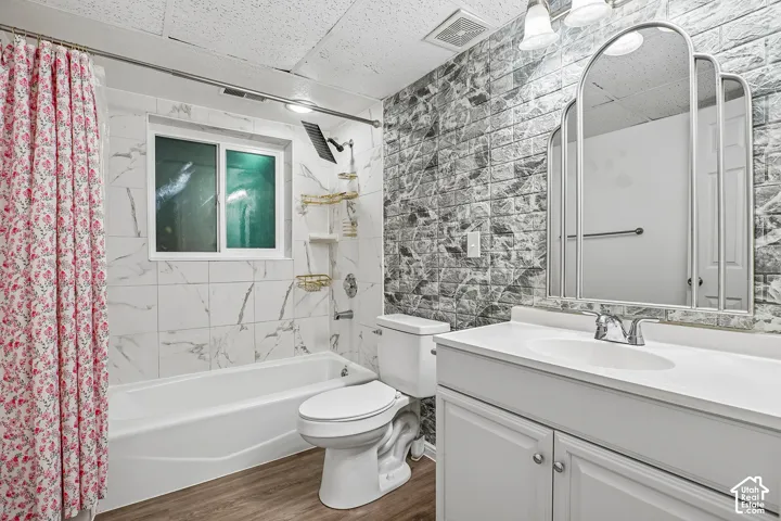 Bathroom featuring a white vanity with integrated sink, a three-panel arched mirror, a bathtub with white tile surround, and wood-finish flooring