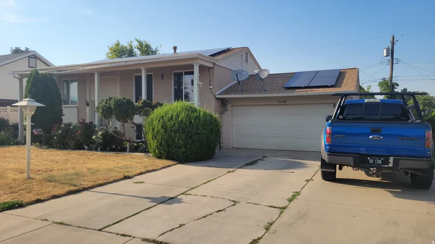 Single-story residence featuring a covered front porch, attached garage, and solar panels