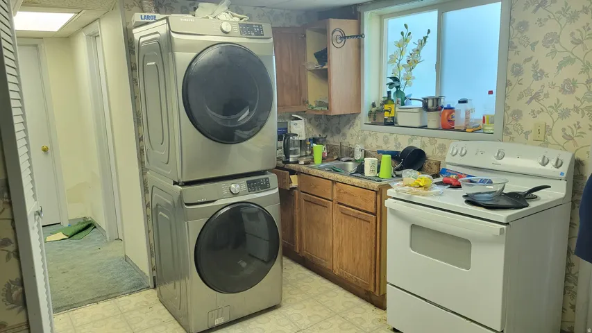 Built-in stackable washer and dryer, white electric range, wood-finish cabinetry, and a single-basin sink