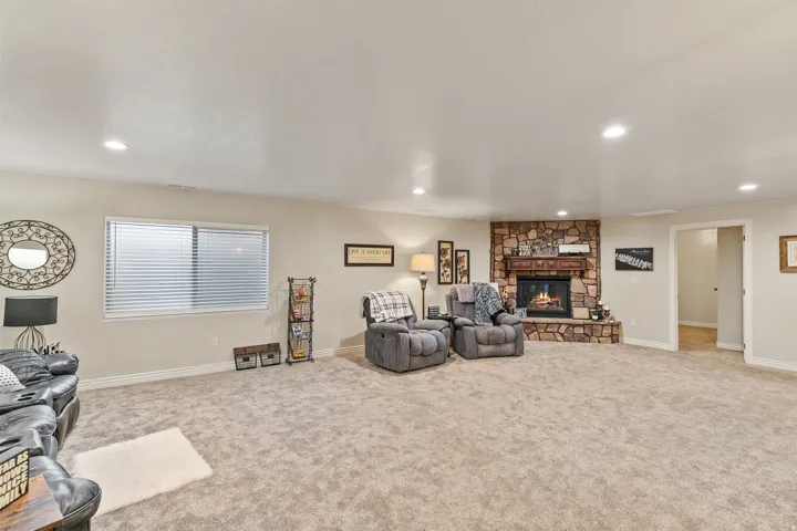 Spacious room featuring neutral carpeting, recessed lighting, a stone-surround fireplace with a wood mantle, and a window with blinds