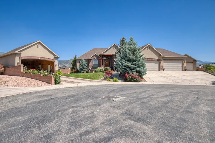 Stucco exterior with brick accents, prominent two-car garage, separate auxiliary garage structure, mature landscaping, and concrete driveways