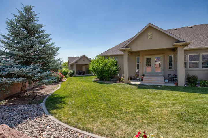 Expansive rear yard with a manicured lawn, established landscaping, and a covered patio with columns