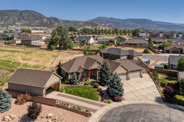 Expansive concrete driveway, attached two-car garage, manicured front lawn, detached garage with extended driveway, and brick retaining walls