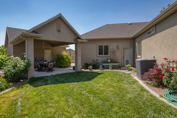 Expansive backyard featuring a covered patio, manicured lawn, and mature landscaping