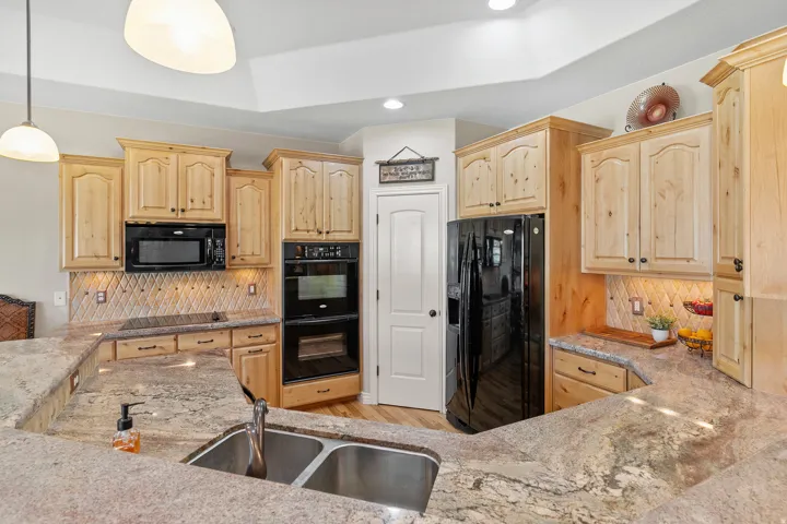 Kitchen featuring light wood cabinetry, stone countertops, a double basin sink, and black appliances including a built-in oven and microwave