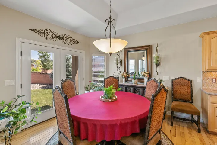 Tray ceiling with a decorative pendant light fixture, French doors opening to a backyard, wood-finish flooring, and built-in cabinetry with a tiled backsplash