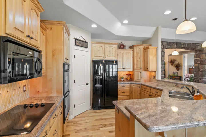 Kitchen featuring wood cabinetry, stainless steel double basin sink, stone countertops, and wood-finish flooring
