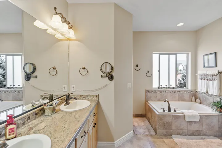 Dual sink vanity with stone-finish countertop, undermount sinks, and wall-mounted light fixture