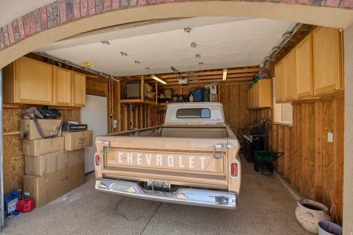 Attached garage with overhead door, built-in cabinetry, exposed wood-panel walls, and concrete flooring