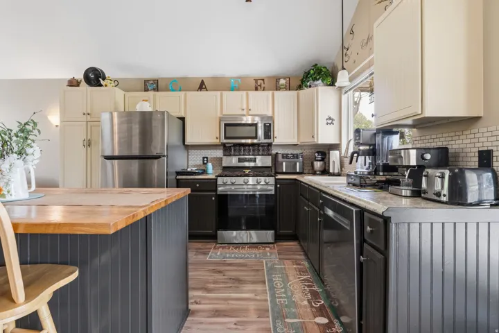 Kitchen featuring wood-finish flooring, two-tone cabinetry, stainless steel appliances, a tile backsplash, and a central island with a wood countertop