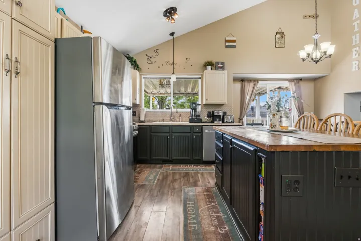 Angled ceiling with pendant lighting, stainless steel refrigerator, wood-finish flooring, built-in kitchen island with wood countertop, and built-in cabinetry