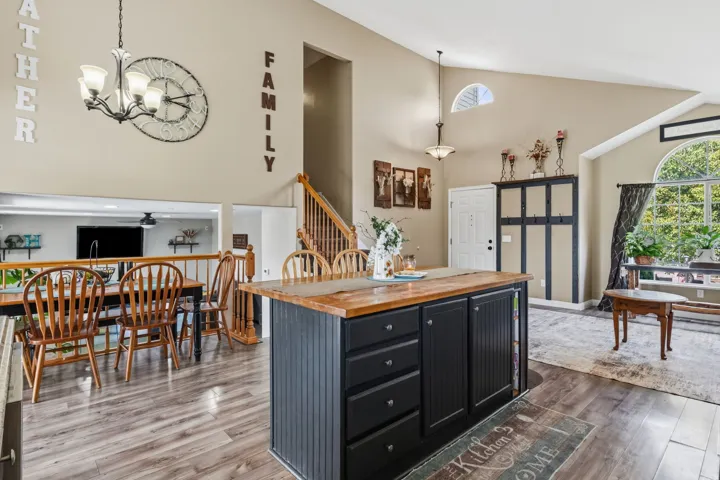 Kitchen island with wood countertop and black cabinetry, vaulted ceiling, arched window, wood-finish flooring, and a wooden staircase