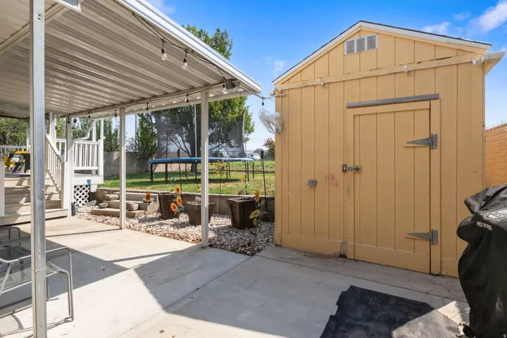 Covered patio with string lighting, concrete flooring, and a separate storage shed
