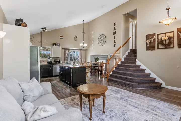 Vaulted ceiling with a wood-finish flooring, kitchen island with built-in storage, and a carpeted staircase with wood railing