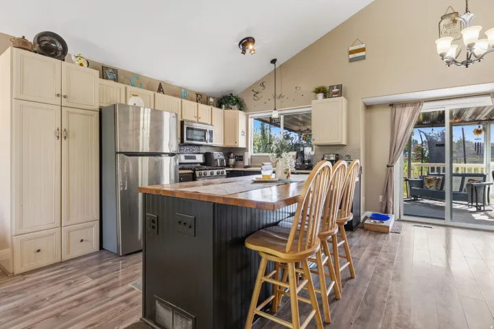 Kitchen featuring vaulted ceilings, wood-finish flooring, stainless steel appliances, a kitchen island with seating, and sliding glass doors to the exterior