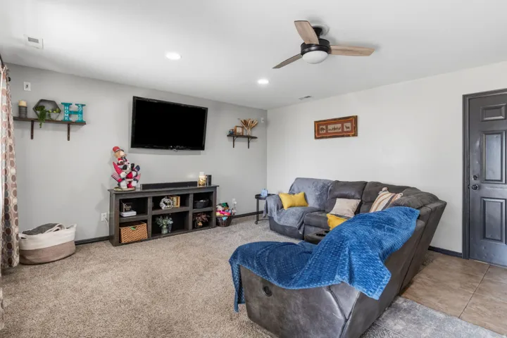 Recessed lighting, ceiling fan with light fixture, wall-mounted shelving, wood-finish media console, and a paneled entry door