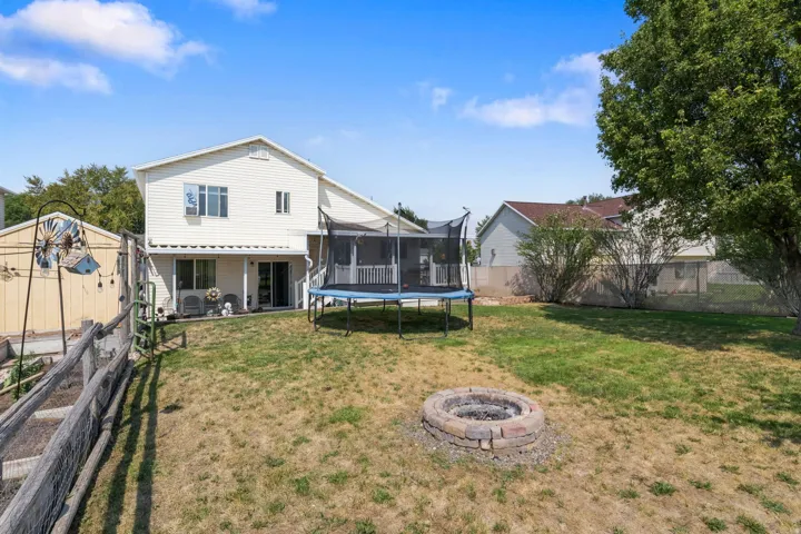 Expansive backyard featuring a stone-ringed fire pit, mature trees, and a covered patio with sliding glass doors