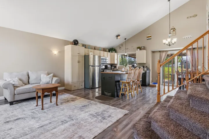 Vaulted ceilings, wood-finish flooring, stainless steel appliances, kitchen island with seating, and a wood staircase with balusters