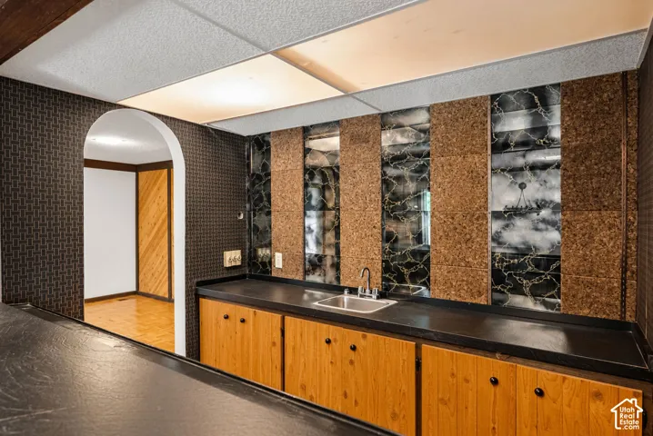 Built-in wet bar featuring a stainless steel sink, wood cabinetry, and a dark countertop