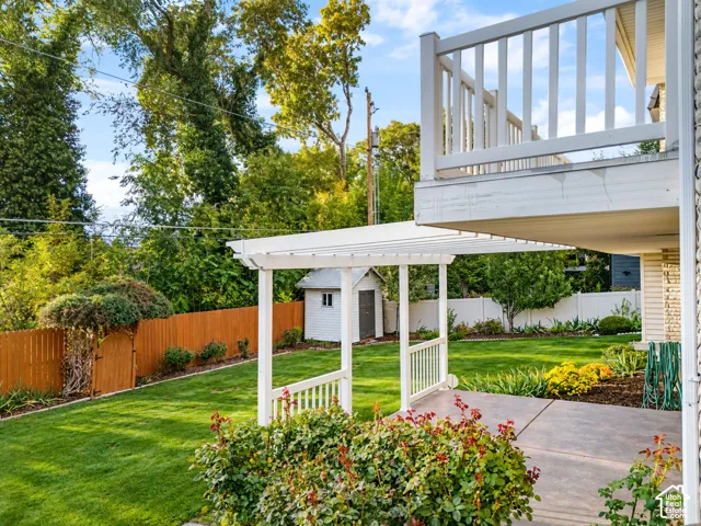 Expansive lawn area with a white pergola-covered patio, mature perimeter trees, a wood privacy fence with a gate to the creek, and a garden shed