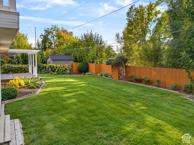 Expansive lawn area, wood privacy fencing, decorative landscaping, built-in storage shed, and a covered patio area