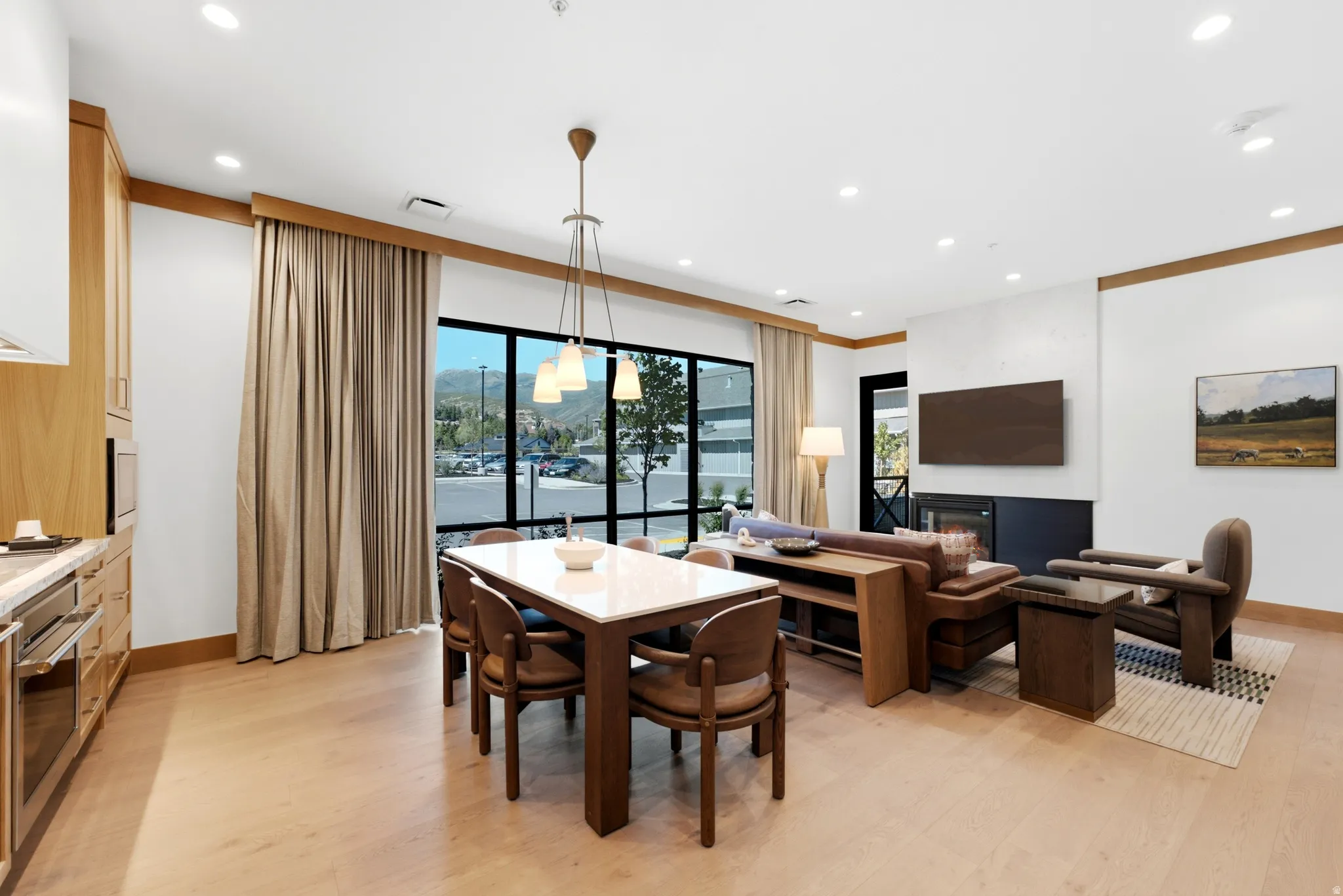 Open-concept living space featuring wood-finish flooring, recessed lighting, a modern built-in fireplace, and expansive windows