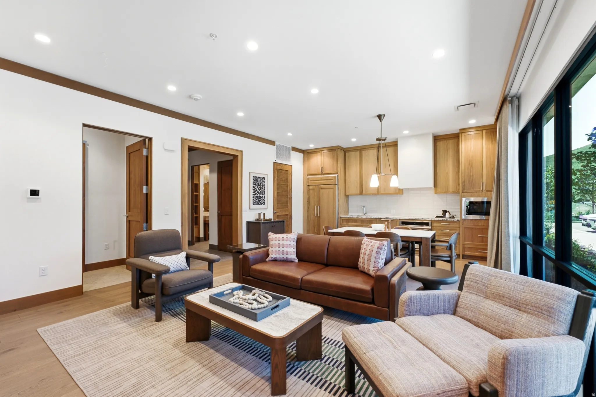 Open-concept living space with wood-finish flooring, recessed lighting, a modern kitchen with built-in appliances, and expansive windows