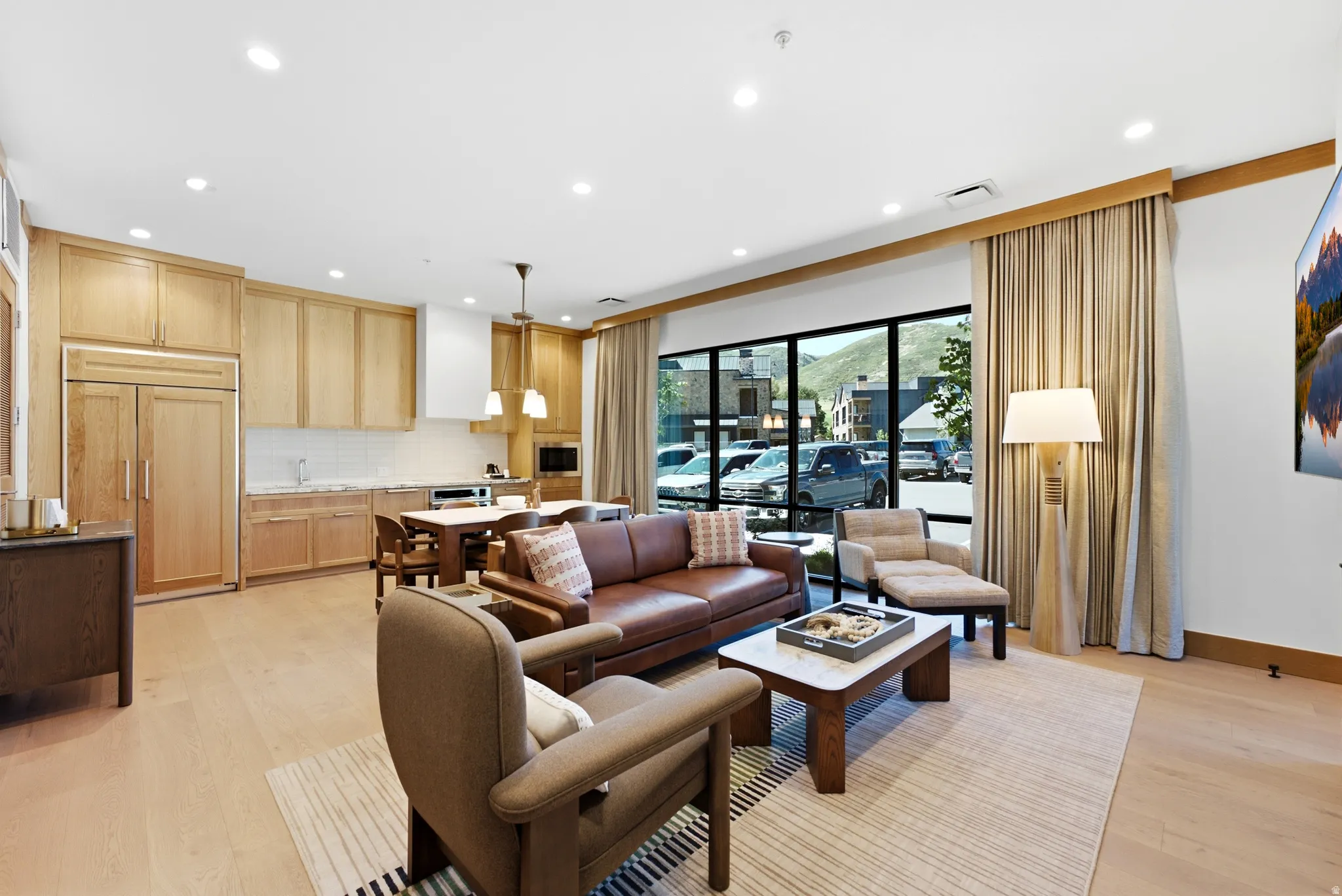 Open-concept living area featuring wood-finish flooring, recessed lighting, expansive windows, and a built-in kitchen with wood cabinetry and panel-front appliances
