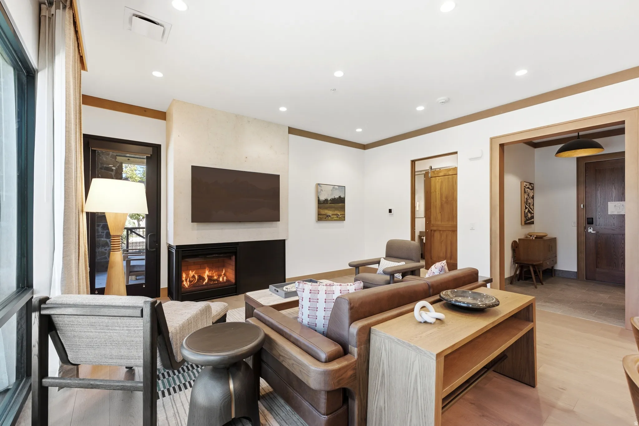 Living area with light wood-finish flooring, a contemporary fireplace, a substantial window, and recessed lighting