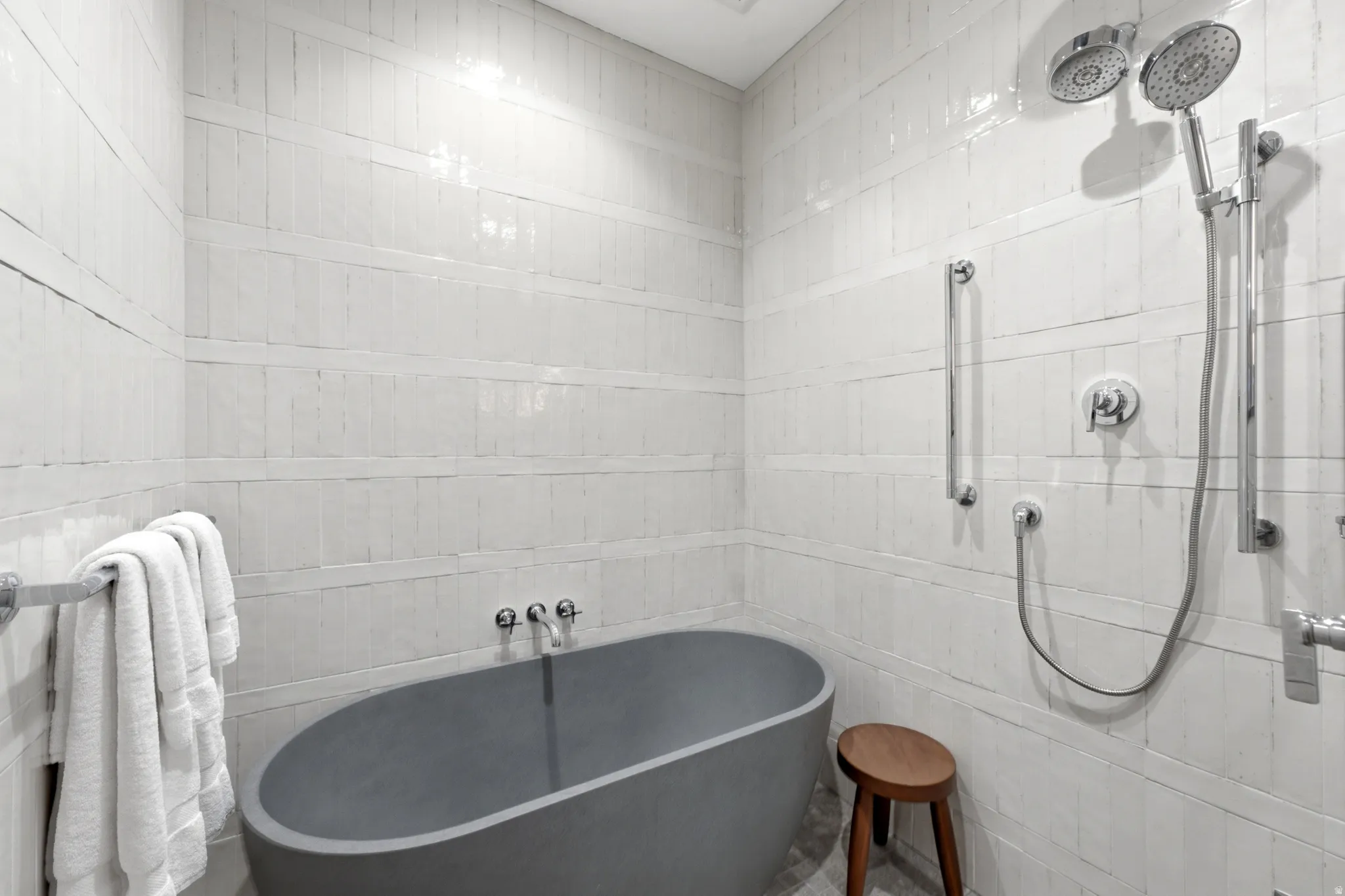 Freestanding soaking tub, floor-to-ceiling tile surround, dual shower heads, and chrome fixtures
