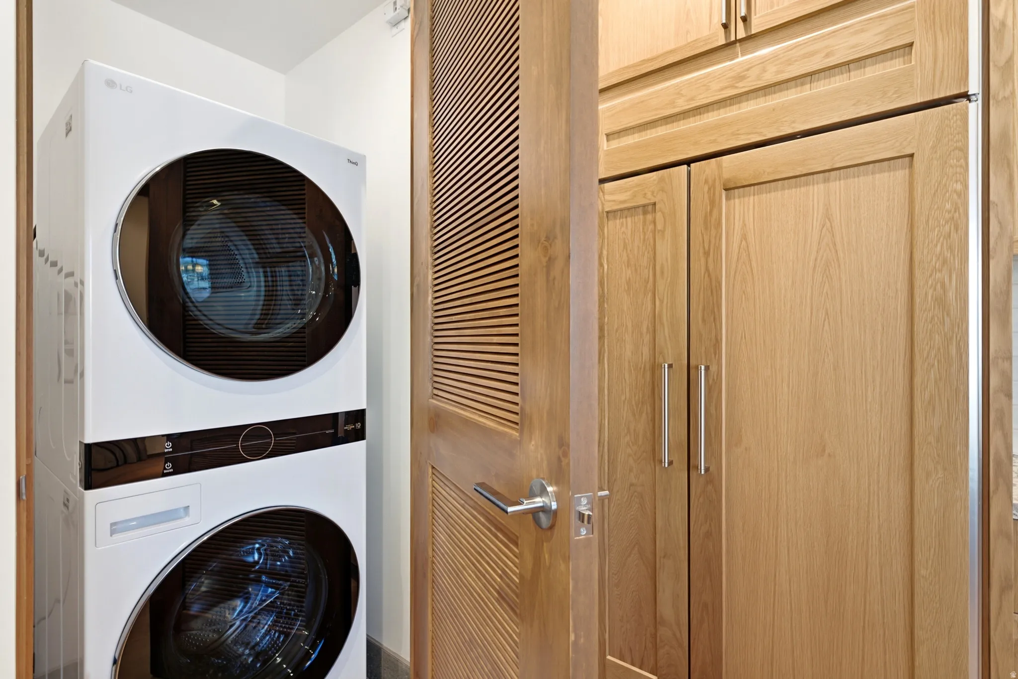 Stacked washer and dryer unit, wood-finish cabinetry, louvered wood-finish door, satin nickel door hardware, stainless steel cabinet pulls