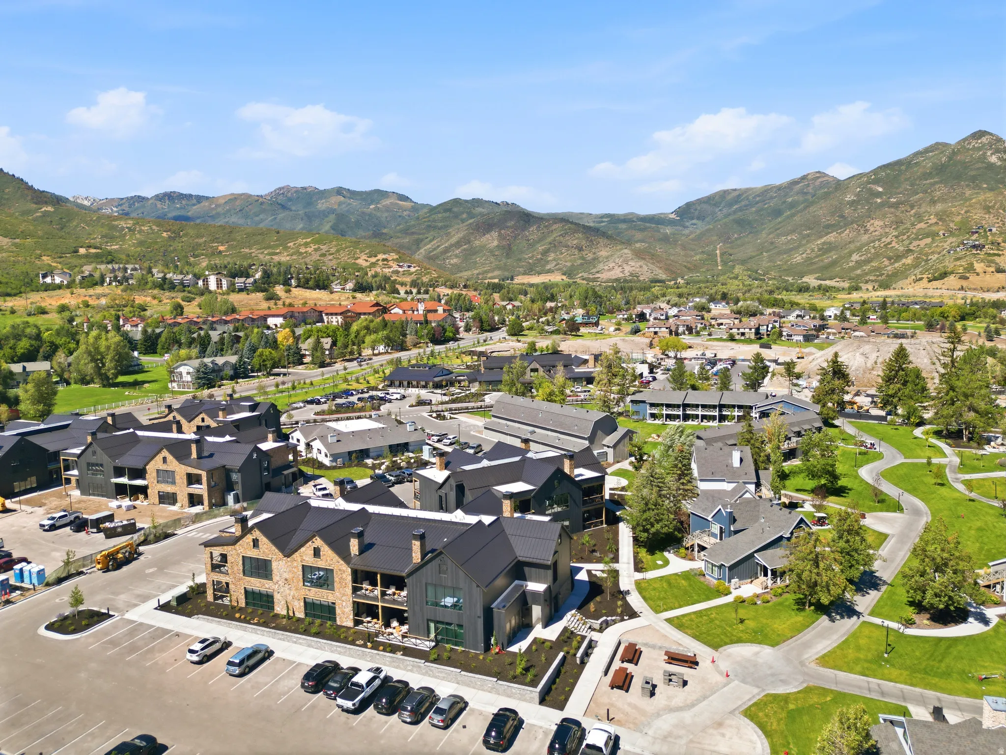 Mountainous landscape with expansive green spaces, paved pathways, and multiple contemporary buildings featuring stone and dark siding