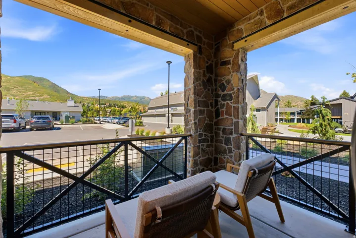 Balcony featuring stone columns, a wood-finish ceiling, and a black metal railing